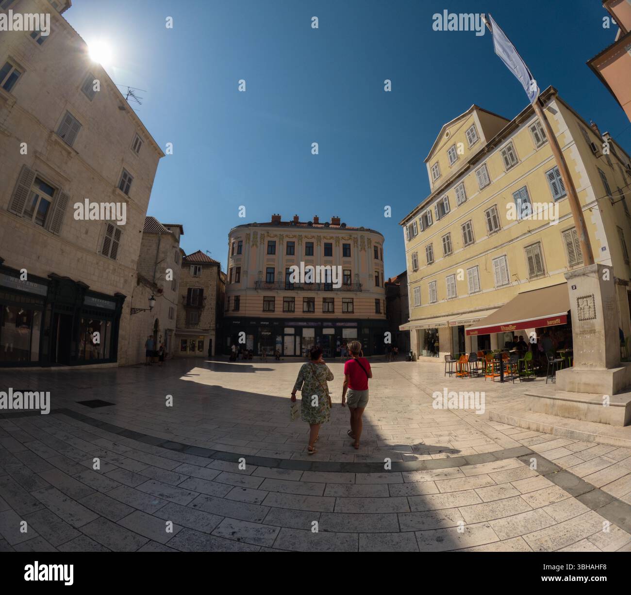 Spalato, Croazia - 8 settembre 2023: Due turisti passeggiano in una piazza illuminata dal sole, esplorando negozi e caffetterie nel centro storico della città. Foto Stock