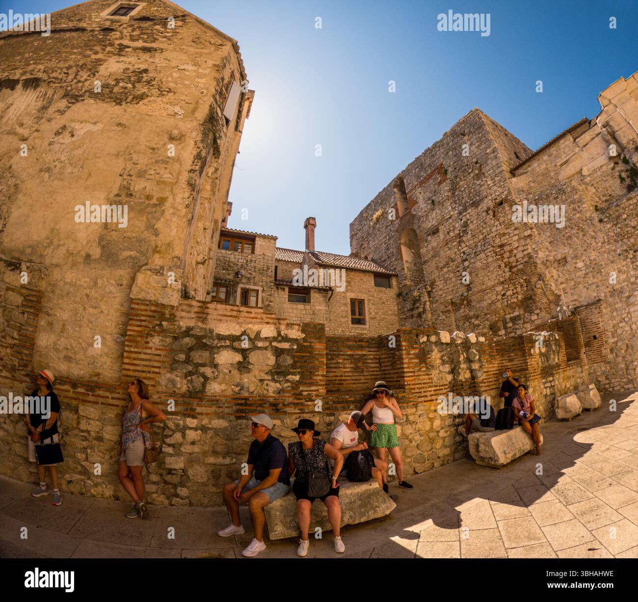 Spalato, Croazia - 8 settembre 2023: I turisti fanno una pausa dall'esplorazione del Palazzo di Diocleziano, seduti e in piedi all'ombra delle antiche mura. Foto Stock