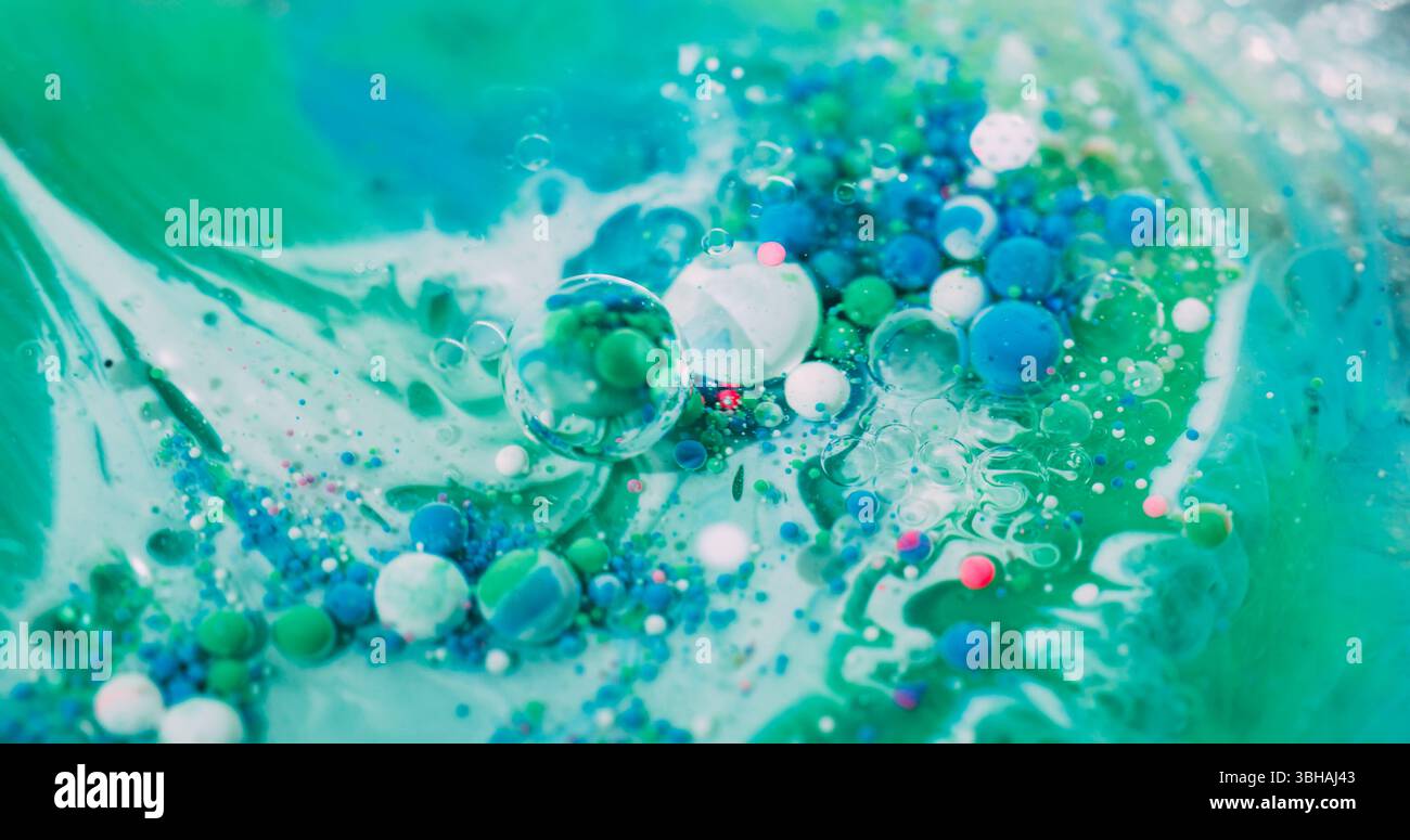 Emulsione a goccia. Bolla di vernice a olio. La sfera acrilica colorata scorre in liquido verde. Le particelle blu brillanti Art Wave mescolano uno sfondo astratto sfocato. Foto Stock