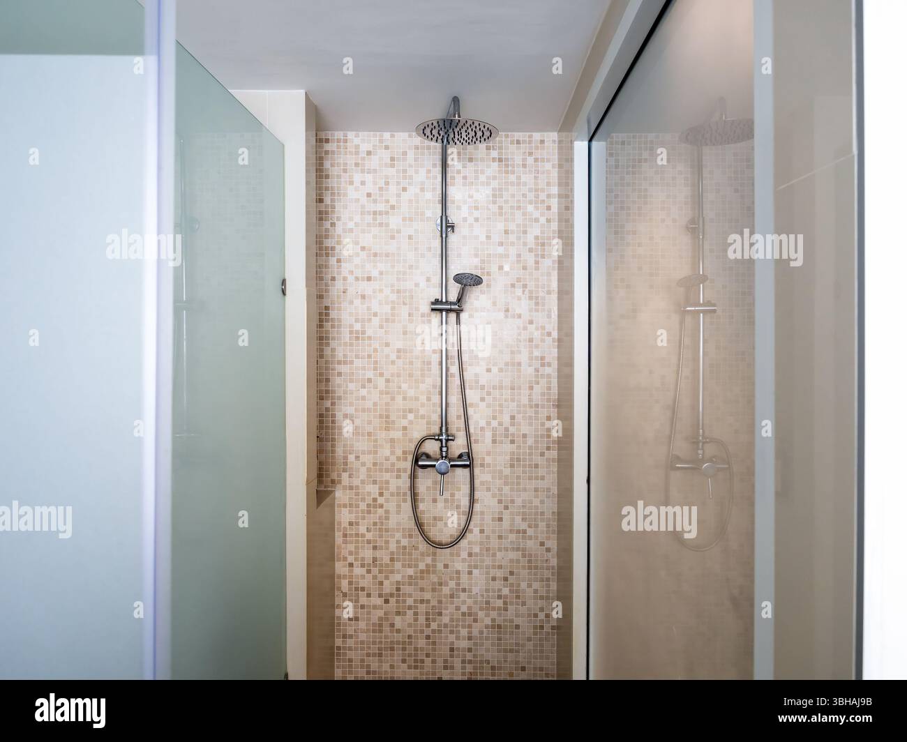 Doccia cromata con doccia a pioggia a soffitto su pareti in piastrelle a mosaico a griglia marrone, decorazione all'interno di una moderna cabina doccia in vetro smerigliato Foto Stock