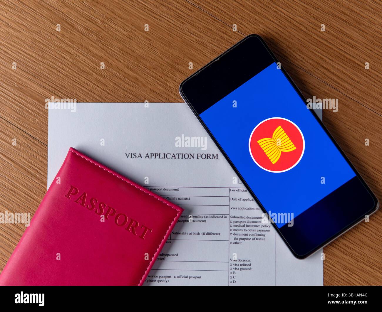Un passaporto, un modulo per la richiesta di visto e uno smartphone che mostra la bandiera ASEAN su un tavolo di legno. Concetto di viaggi internazionali e collegamenti globali Foto Stock