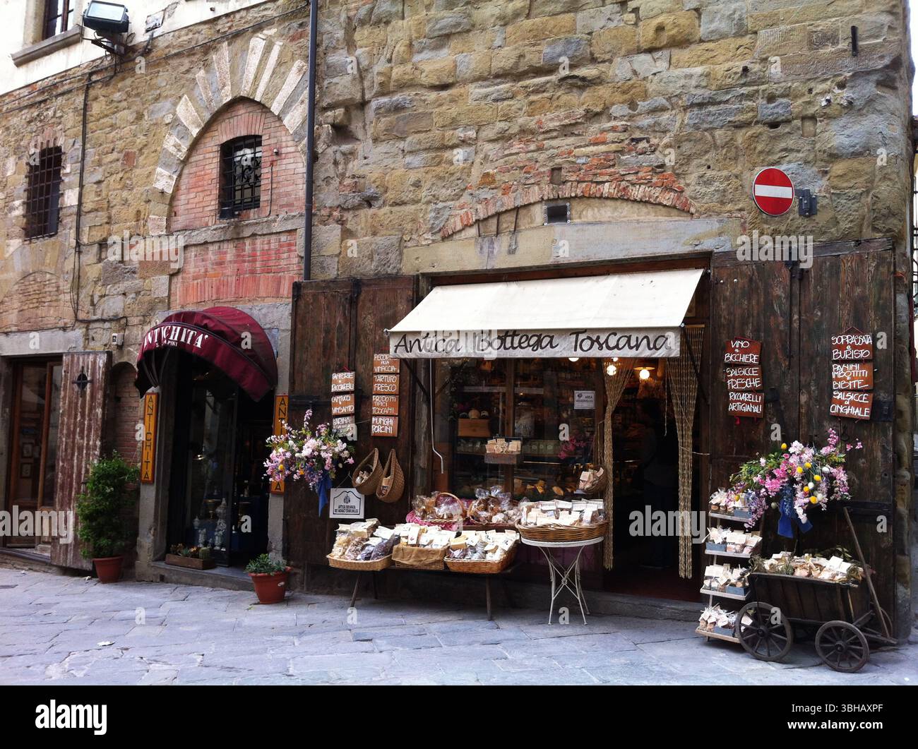 Affascinante strada italiana con negozio Rustic Shopfront e esposizione di prodotti tradizionali. Arezzo, Italia Foto Stock