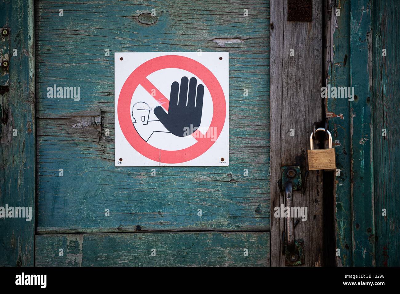 Porta in legno resistente agli agenti atmosferici con vernice turchese sbucciata. Apposto è un simbolo di attenzione: Un simbolo di mano nera all'interno di un cerchio rosso con una linea diagonale, indicatina Foto Stock