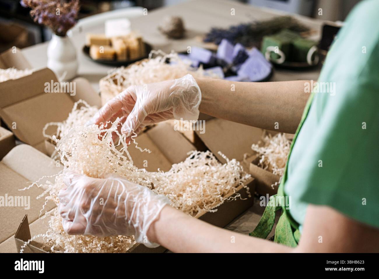 Le mani con i guanti consentono di disporre saponi verdi e lavanda con fiori secchi in confezioni kraft. Prodotti artigianali, imballaggi ecologici, prodotti per la cura della pelle naturali Foto Stock