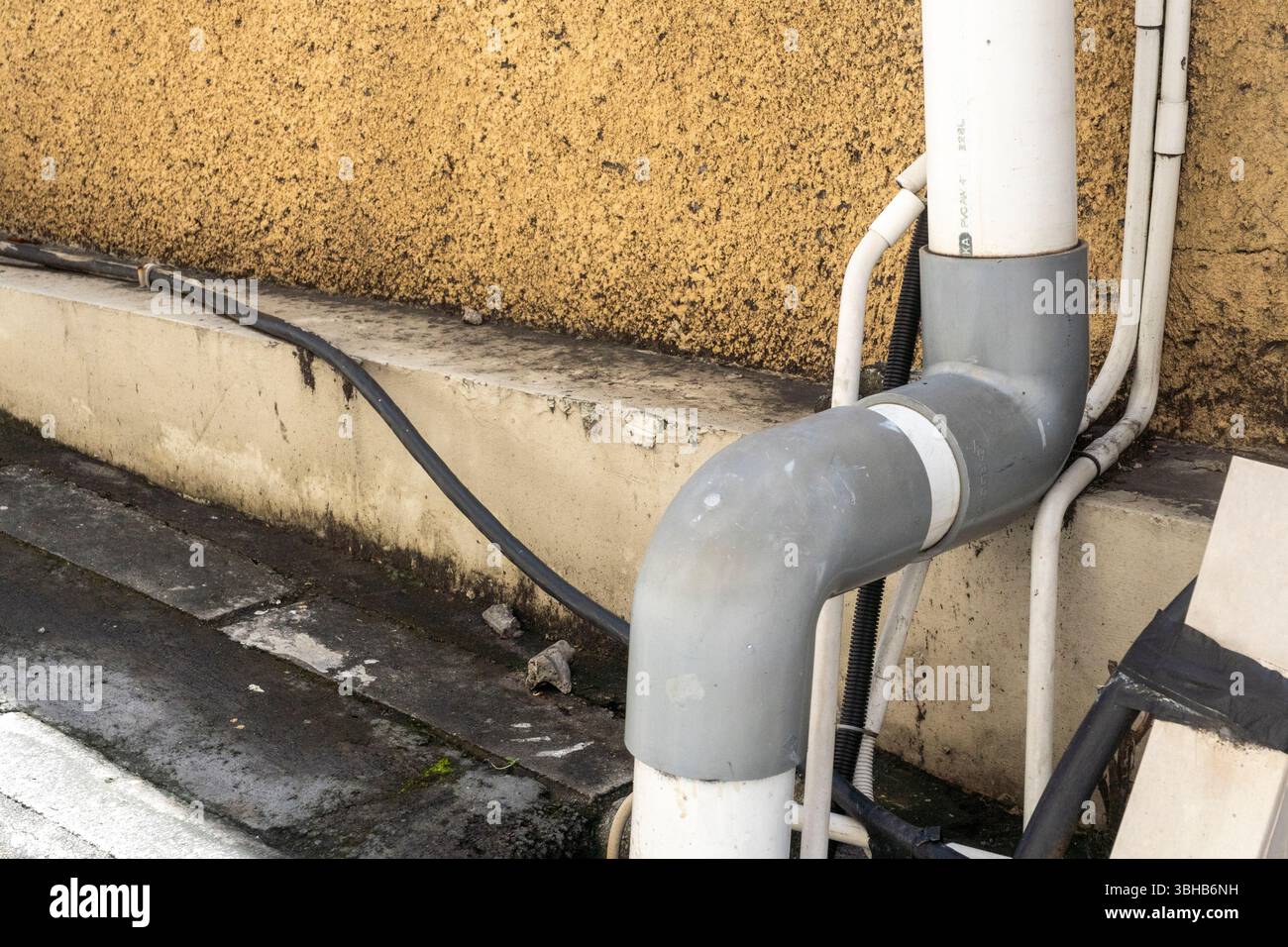 Il tubo è collegato a una parete. Il tubo è bianco e grigio. Il muro è abbronzato Foto Stock