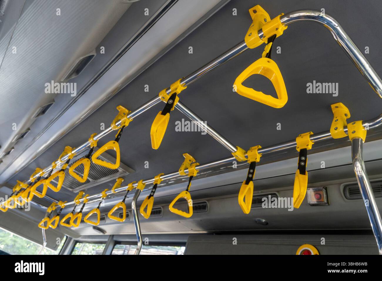 L'autobus ha maniglie gialle su cui i passeggeri possono agganciarsi. Le maniglie sono fissate a una barra di metallo e distanziate uniformemente lungo la lunghezza del trai Foto Stock