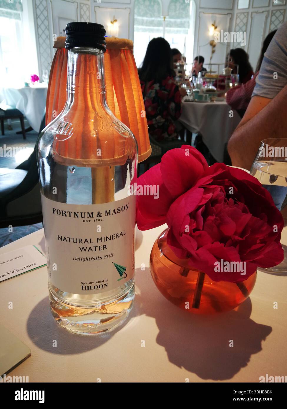 Elegante ambiente da pranzo che mette in risalto la bottiglia d'acqua minerale e la vivace disposizione floreale. Londra, Regno Unito Foto Stock