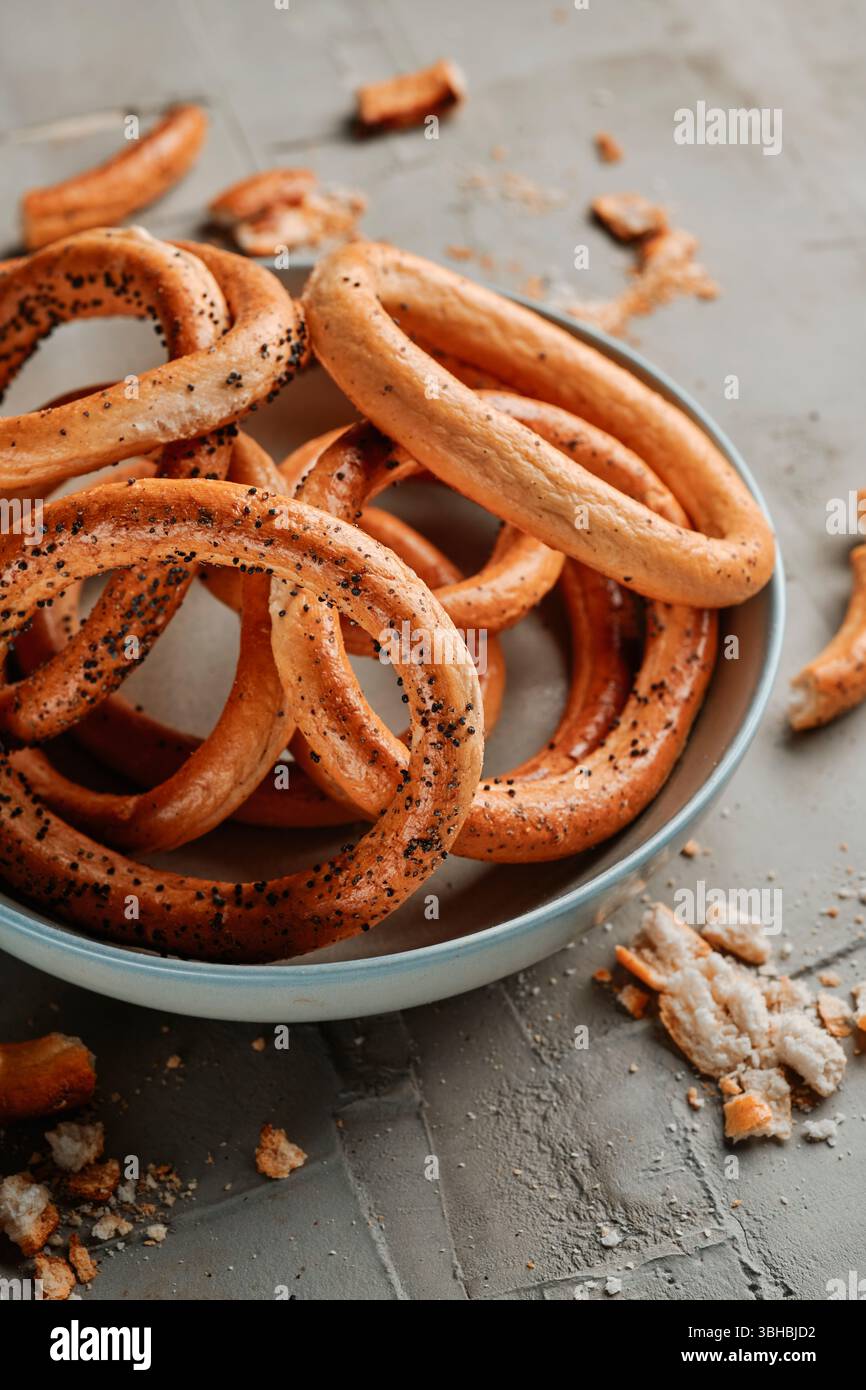 un primo piano di un piatto con alcuni covrigi, anelli di pane rumeni, cosparsi di semi di papavero, posti su una superficie di cemento testurizzato grigio Foto Stock