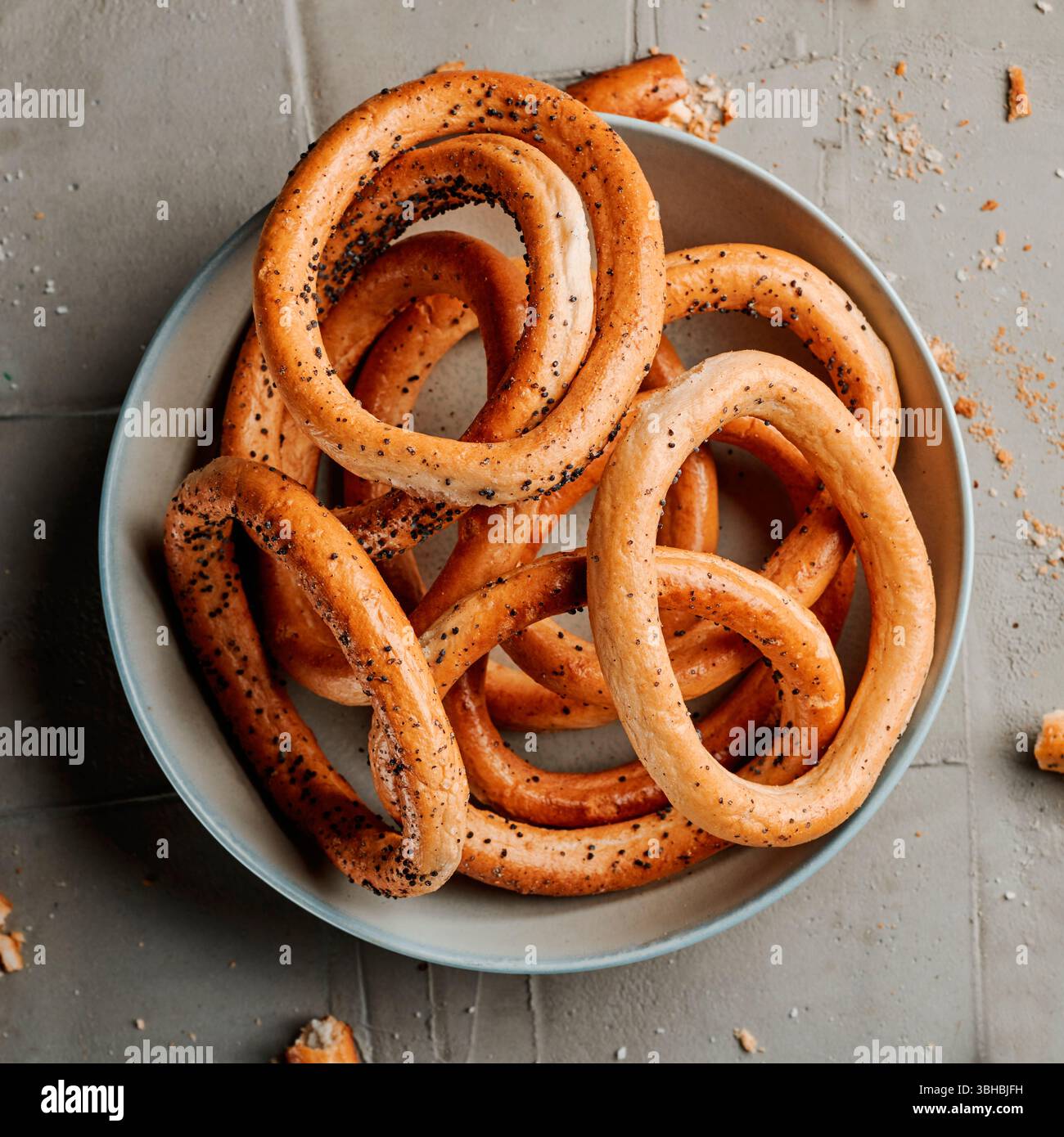 vista ad angolo alto di un piatto con alcuni anelli di pane rumeni, noti come covrigi, cosparsi di semi di papavero, su una superficie grigia in cemento Foto Stock