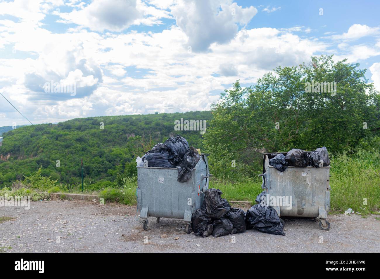 Due contenitori di rifiuti traboccanti con sacchetti neri nell'area verde rurale. Foto Stock