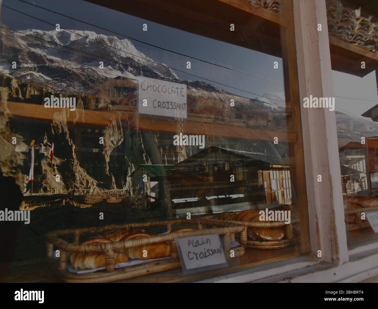 Una finestra di panificio con prodotti da forno al suo interno con un riflesso delle montagne himalayane nel vetro. Le montagne sono innevate e la panetteria è piccola Foto Stock