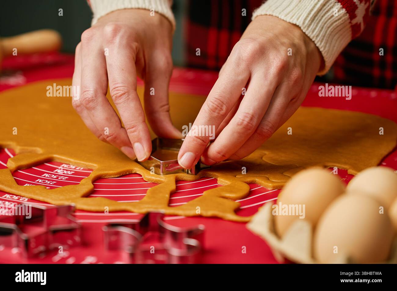 Primo piano delle mani premendo il tagliabasette in metallo nell'impasto di pan di zenzero sul tappetino da forno in silicone. Preparazione al forno per le feste e concetto di tradizione familiare Foto Stock