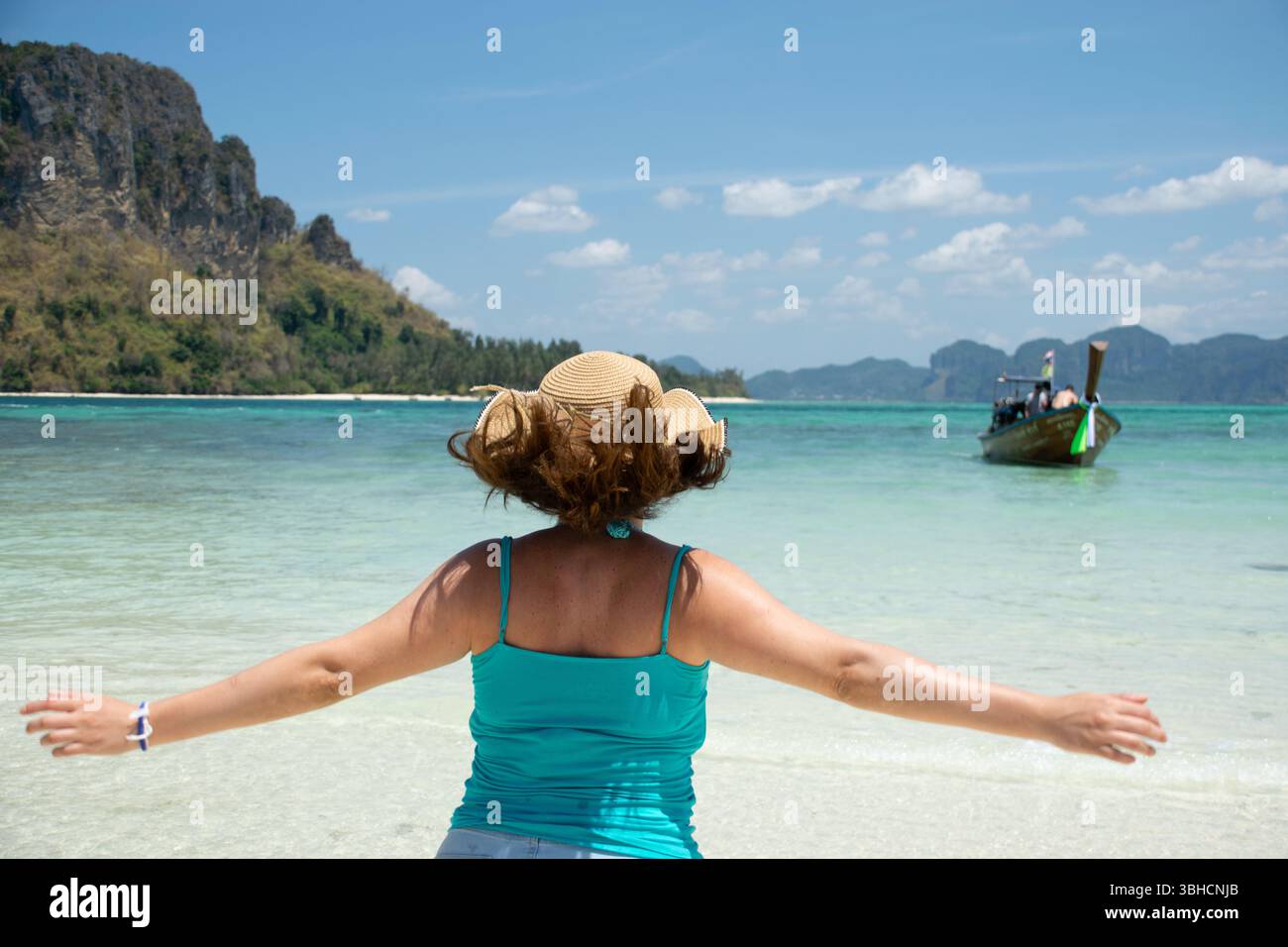 Vista posteriore di una giovane donna che corre e apre le braccia osservando la meravigliosa spiaggia dell'isola di Phi Phi, Thailandia Foto Stock