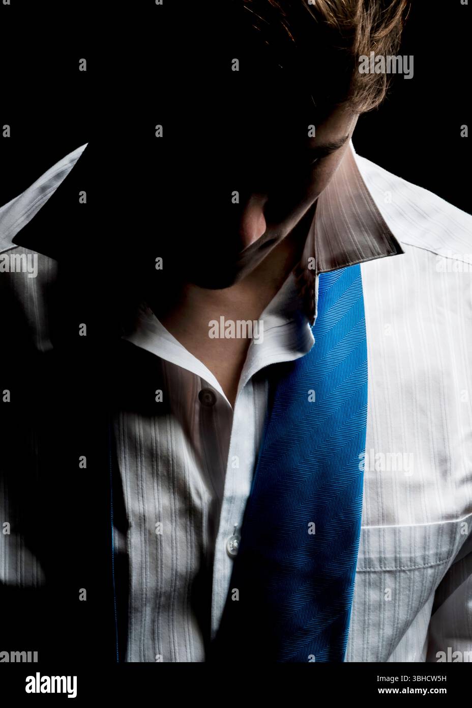 Una persona che indossa una camicia bianca in tessuto e una cravatta blu viene mostrata dal petto verso l'alto. Il volto della persona è oscurato dall'ombra, e sono io Foto Stock