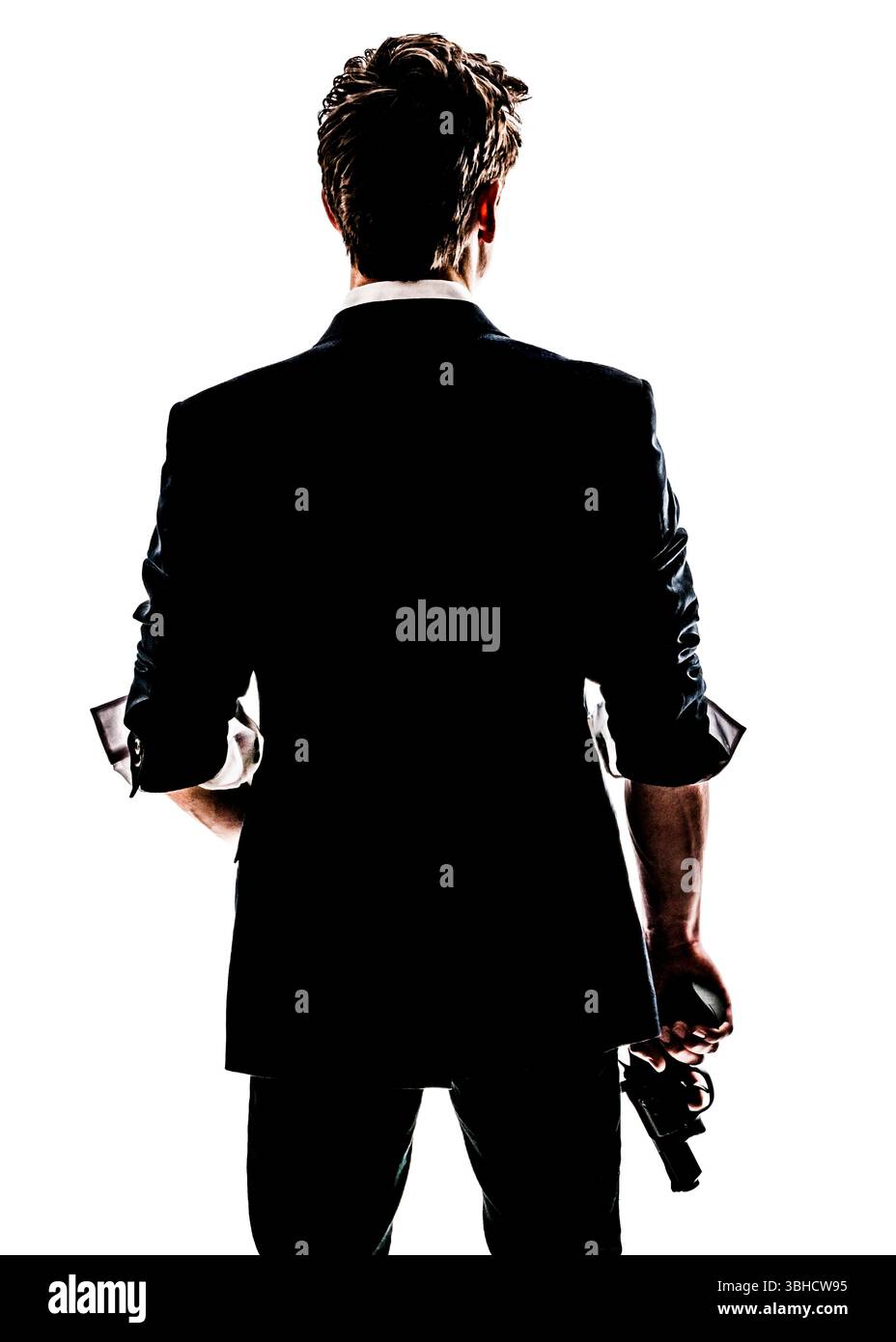 Un uomo con una tuta, visto da dietro, tiene una pistola al suo fianco. L'immagine è una silhouette su uno sfondo bianco, oscurando il suo volto e altri dettagli Foto Stock