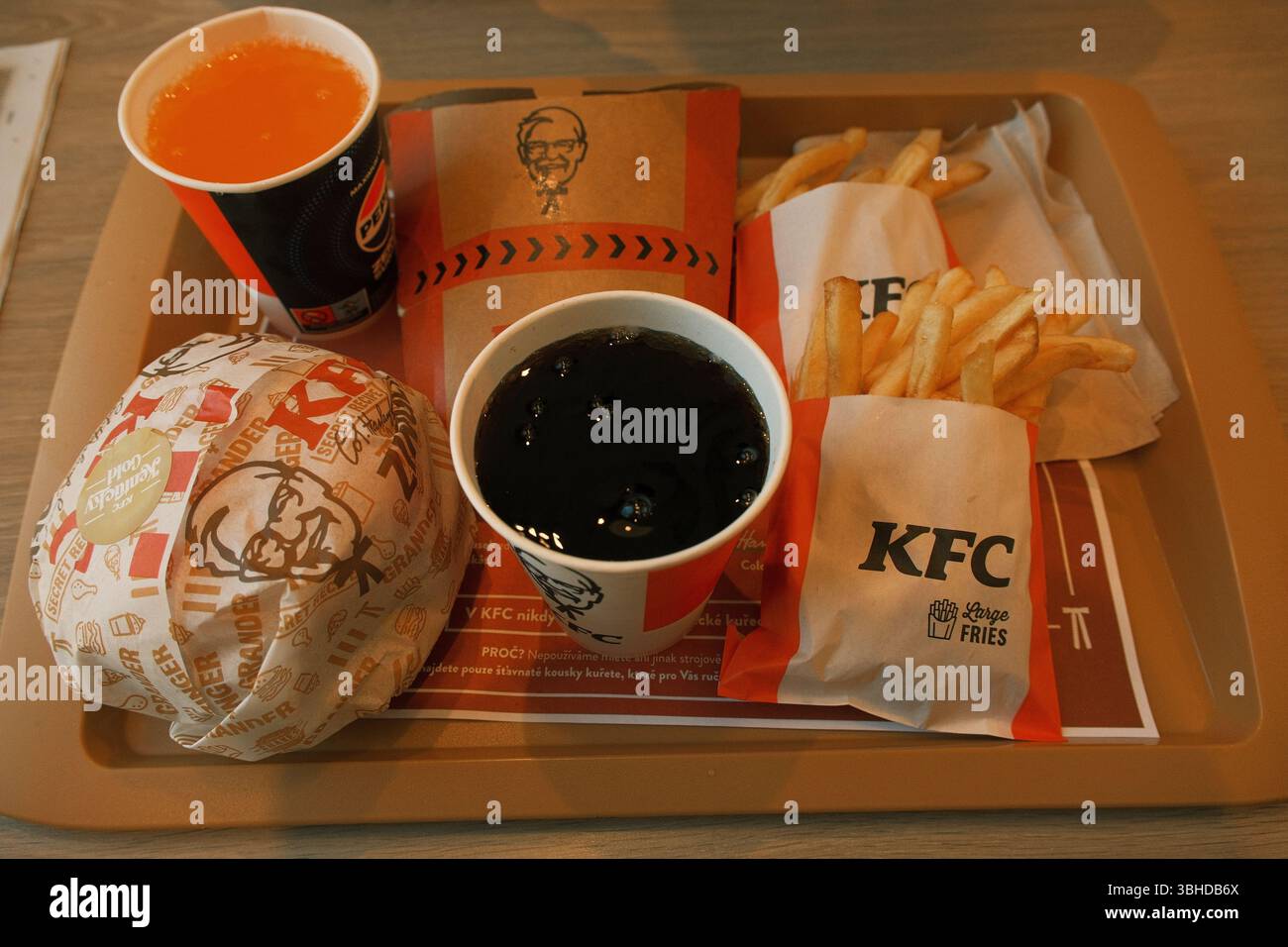 Un classico pasto fast food KFC servito su un vassoio, con due porzioni di patatine fritte, un hamburger di pollo avvolto e due bevande analcoliche. Foto Stock