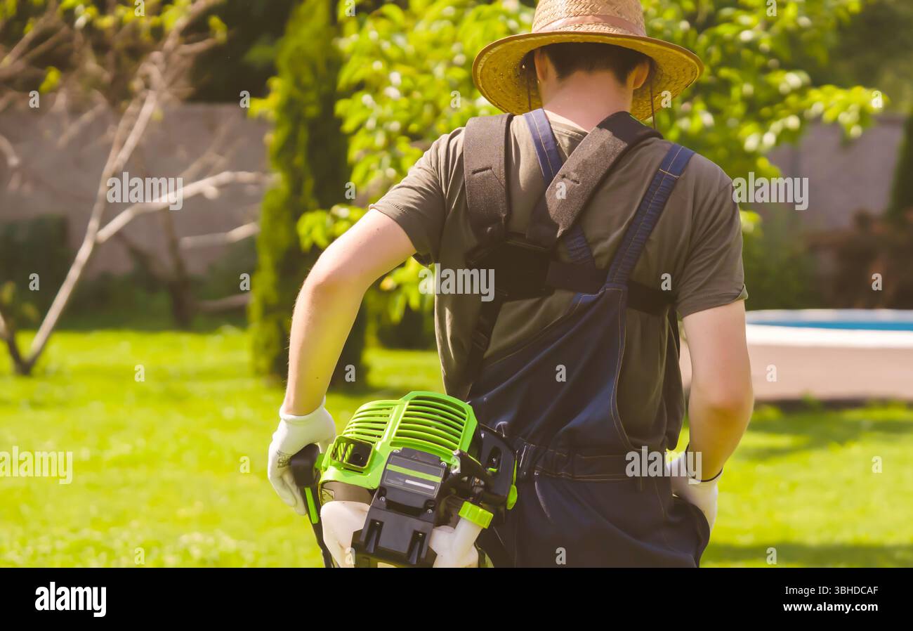 Un uomo con un rasaerba si prende cura dell'erba nel cortile. Foto Stock