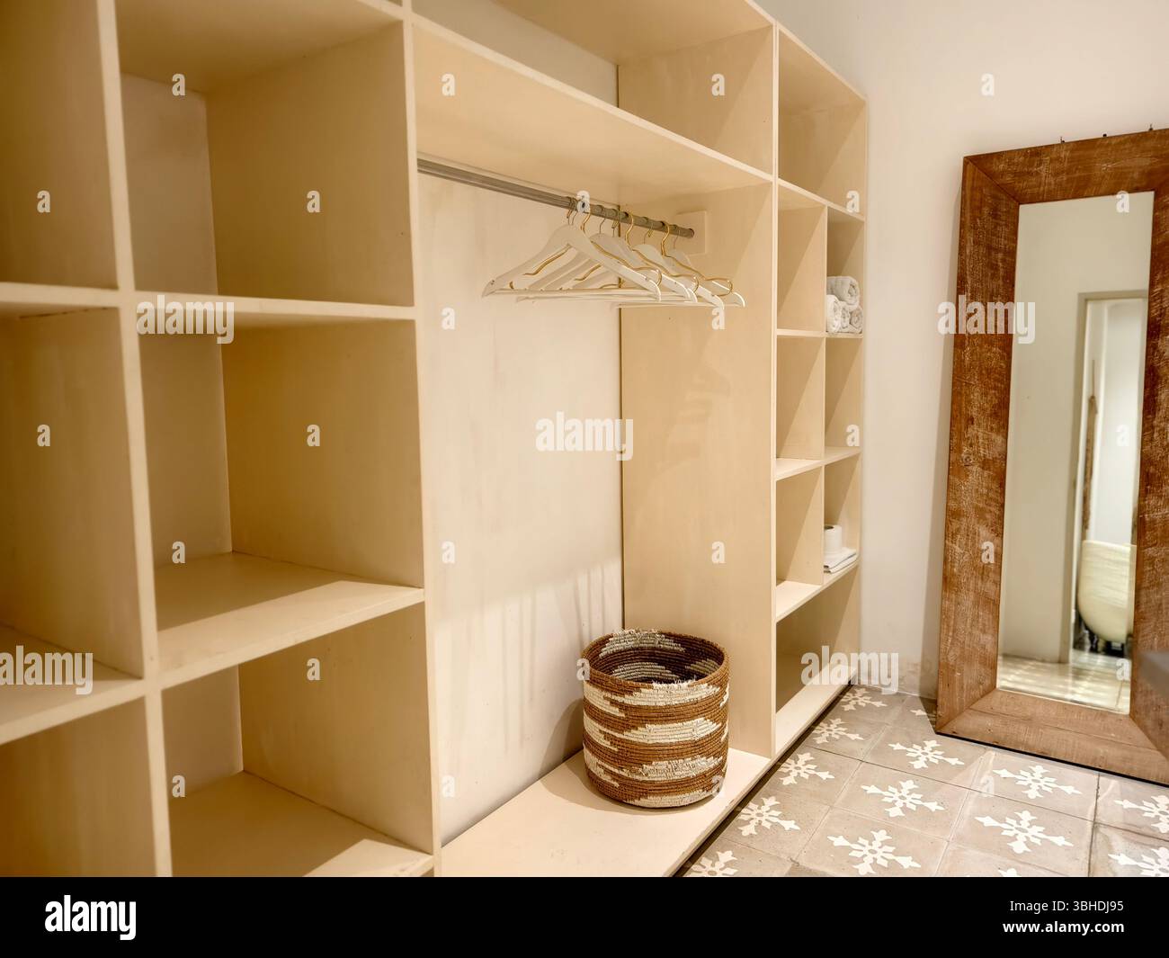 un armadio minimalista con scaffalature aperte, appendiabiti, un cestino intrecciato e un grande specchio rustico Foto Stock