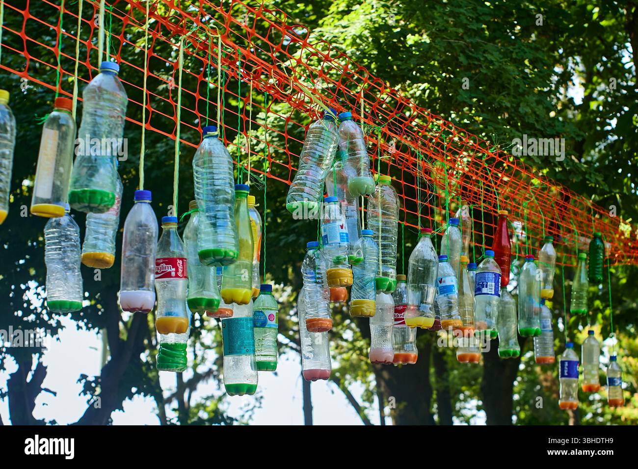 Le bottiglie di plastica sospese su una rete tra gli alberi formano un'installazione ambientale creativa, che sottolinea l'importanza del riciclaggio e del riutilizzo Foto Stock
