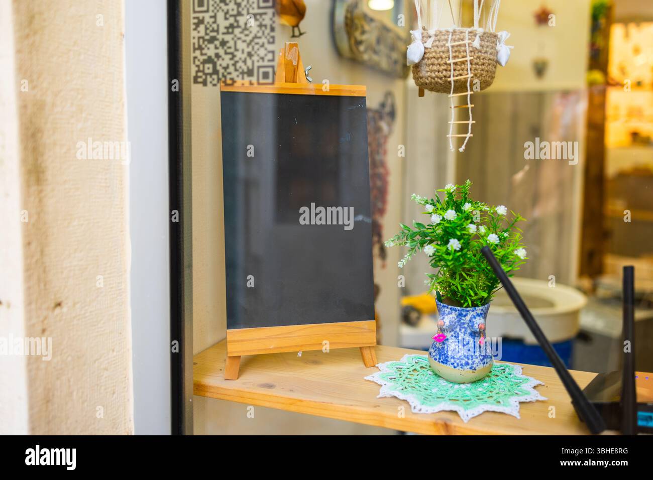 Cartello lavagna vuota con piccola pianta nella finestra davanti al magazzino. Allestimenti creativi, atmosfera accogliente e spazio per messaggi personalizzabili. Foto Stock