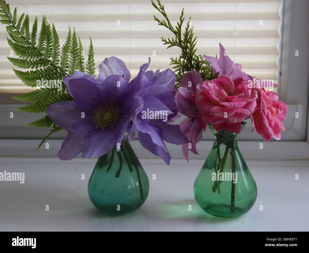 Due piccoli vasi di vetro colorati con semplici esposizioni floreali per mostrare i fiori tagliati da un giardino inglese all'inizio dell'estate. Foto Stock