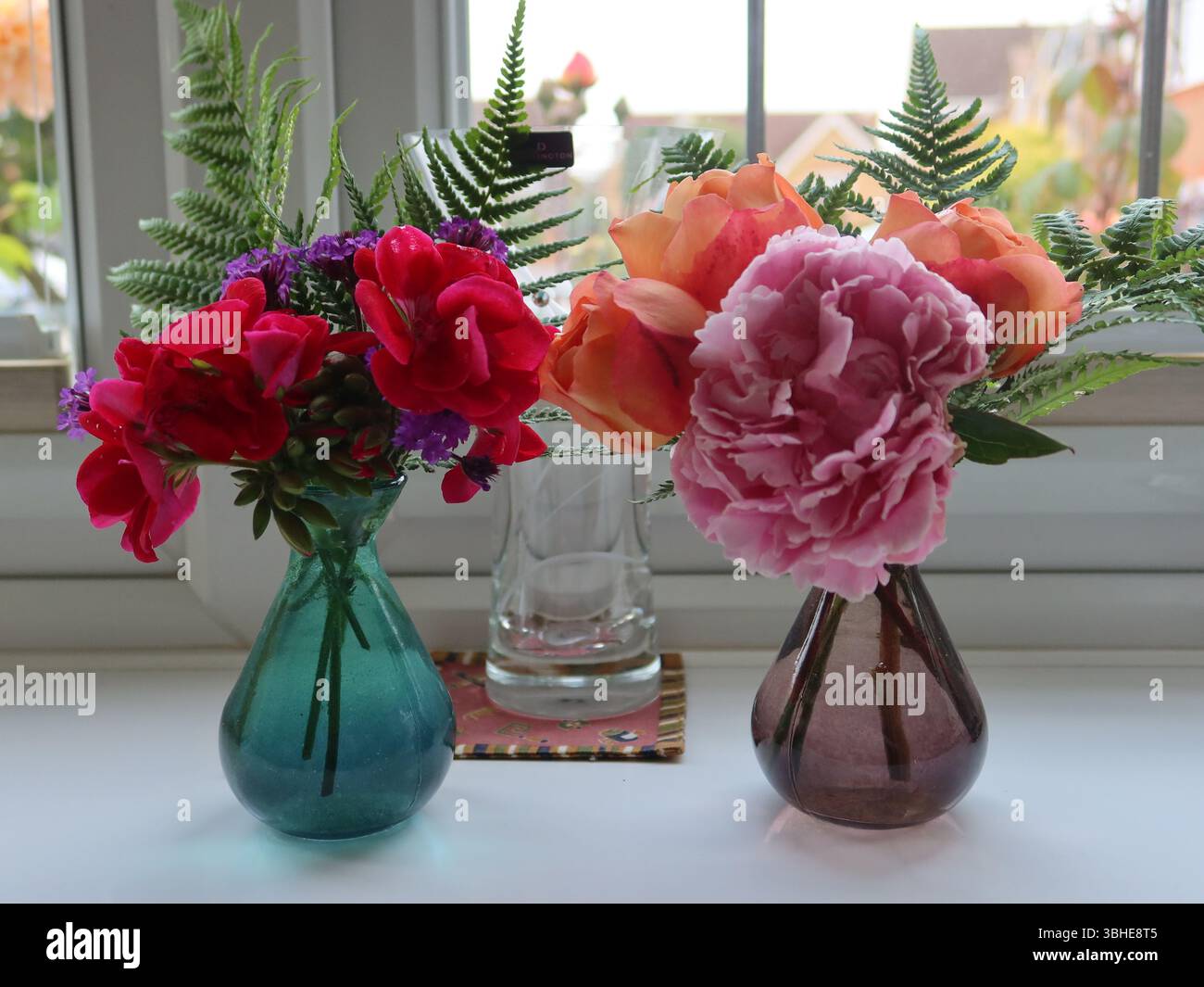Due piccoli vasi di vetro colorati con semplici esposizioni floreali per mostrare i fiori tagliati da un giardino inglese all'inizio dell'estate. Foto Stock
