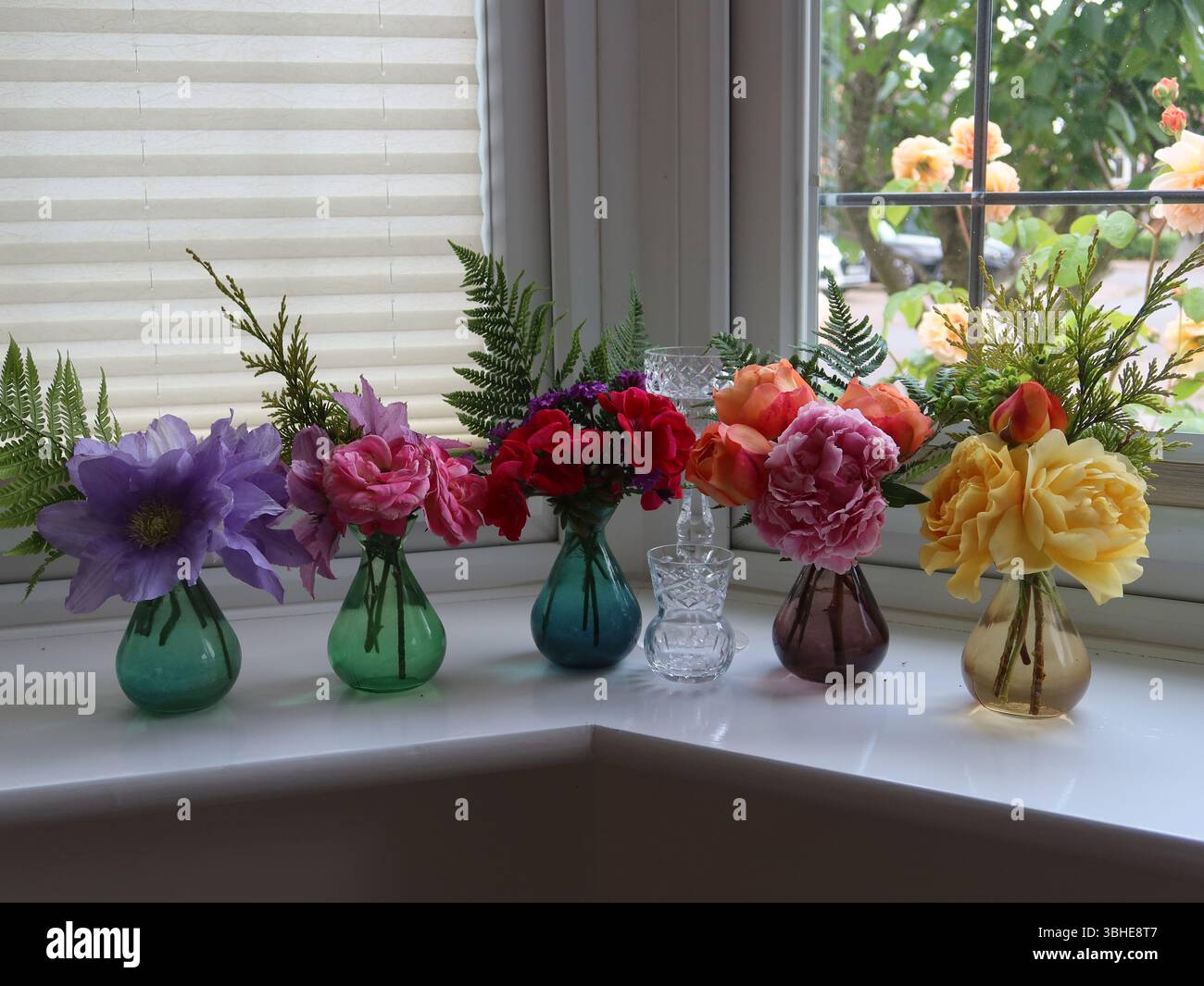 Una fila di 5 piccoli vasi di vetro colorati con la possibilita' di fiori estivi inglesi illuminano un davanzale e creano una bella, ma semplice, esposizione floreale. Foto Stock