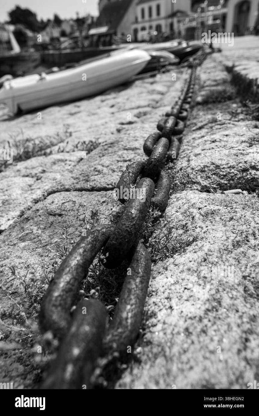 Primo piano di una catena intemprata ancorata a un molo del porto, catturata in una spettacolare prospettiva in bianco e nero. Foto Stock