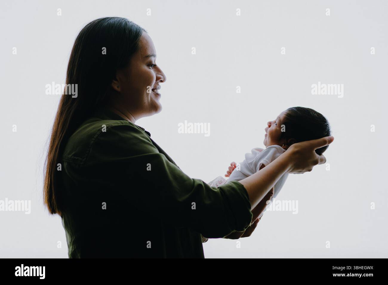 Una madre culla la sua bambina appena nata in uno spazio bianco e delicatamente illuminato. L'immagine esprime amore materno, calore e protezione Foto Stock