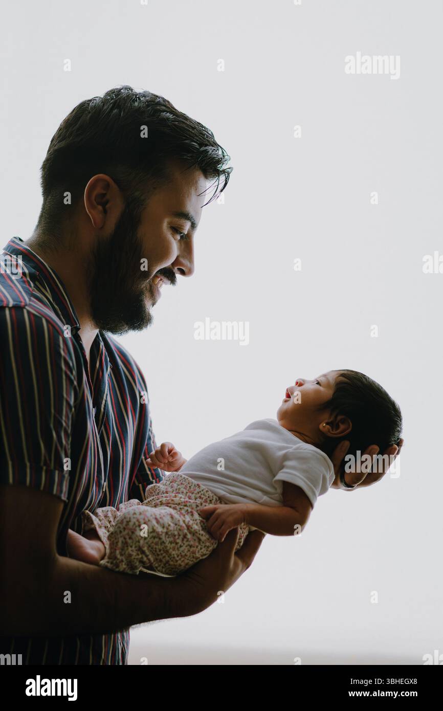 Padre che tiene in braccio la figlia neonata in un abbraccio amorevole con retroilluminazione morbida Foto Stock
