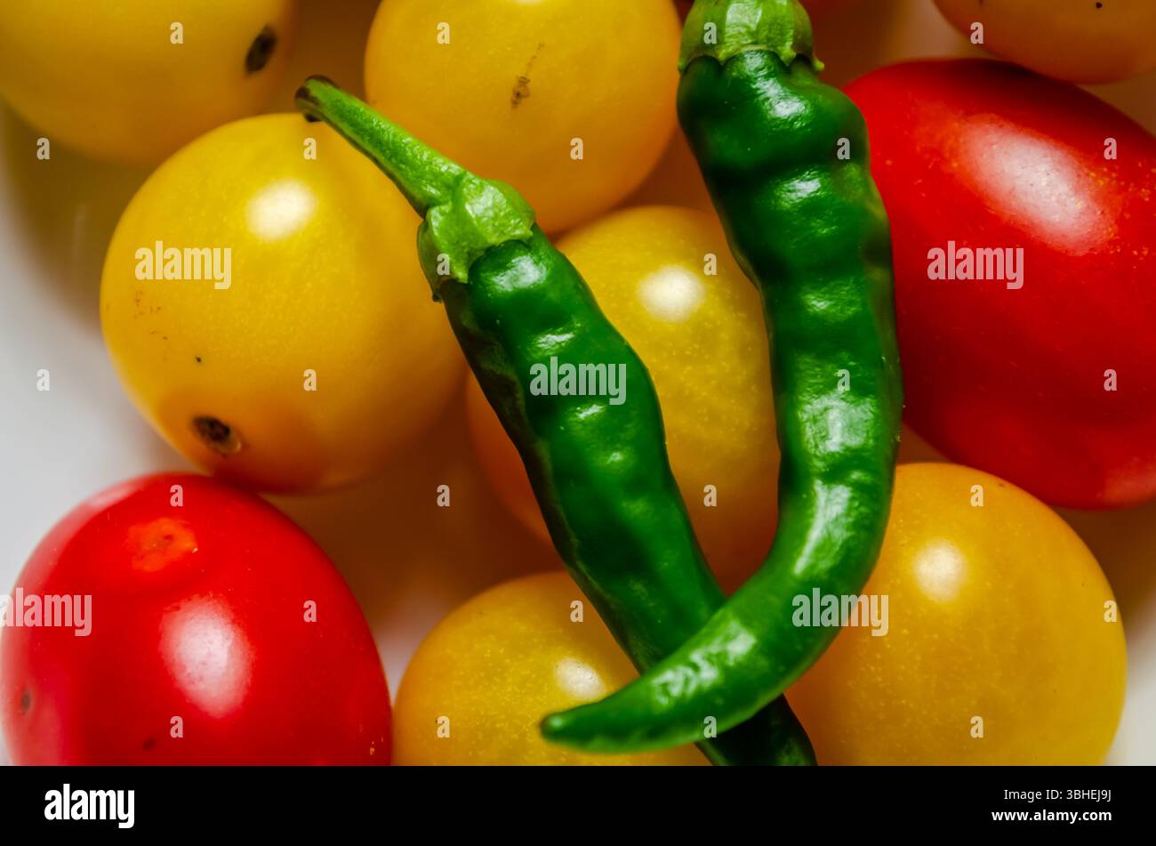 Due peperoncini verdi su pomodori ciliegini gialli e pomodori uva rossa. Foto Stock