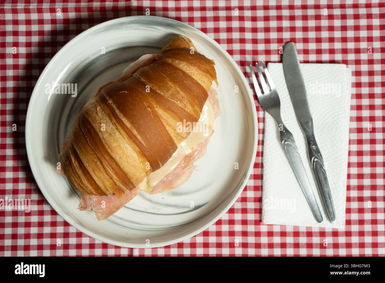 Panino artigianale con croissant al prosciutto e formaggio, tostato alla perfezione e servito su un piatto rustico di legno. Ottimo per la fotografia gastronomica e la bran culinaria Foto Stock