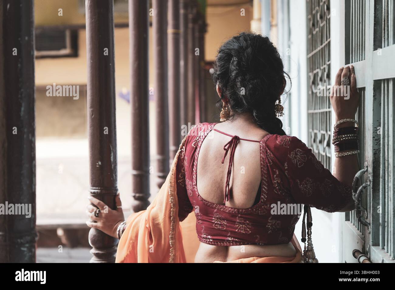 Ritratto di una donna indiana tradizionale che indossa una camicetta rossa e un sari giallo, accessoriato con bracciali, orecchini e un anello per il naso, edificio storico Foto Stock
