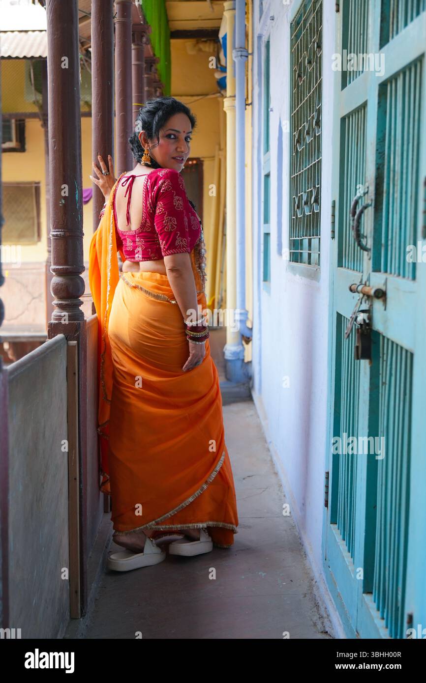 Ritratto di una donna indiana tradizionale che indossa una camicetta rossa e un sari giallo, accessoriato con bracciali, orecchini e un anello per il naso, edificio storico Foto Stock