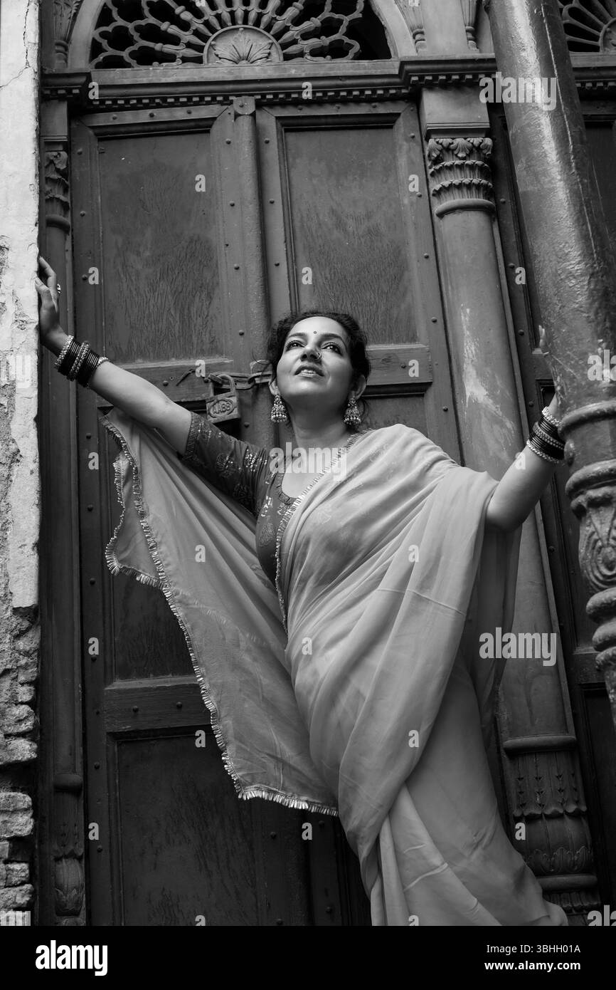 Ritratto di una donna indiana tradizionale che indossa una camicetta rossa e un sari giallo, accessoriato con bracciali, orecchini e un anello per il naso, edificio storico Foto Stock