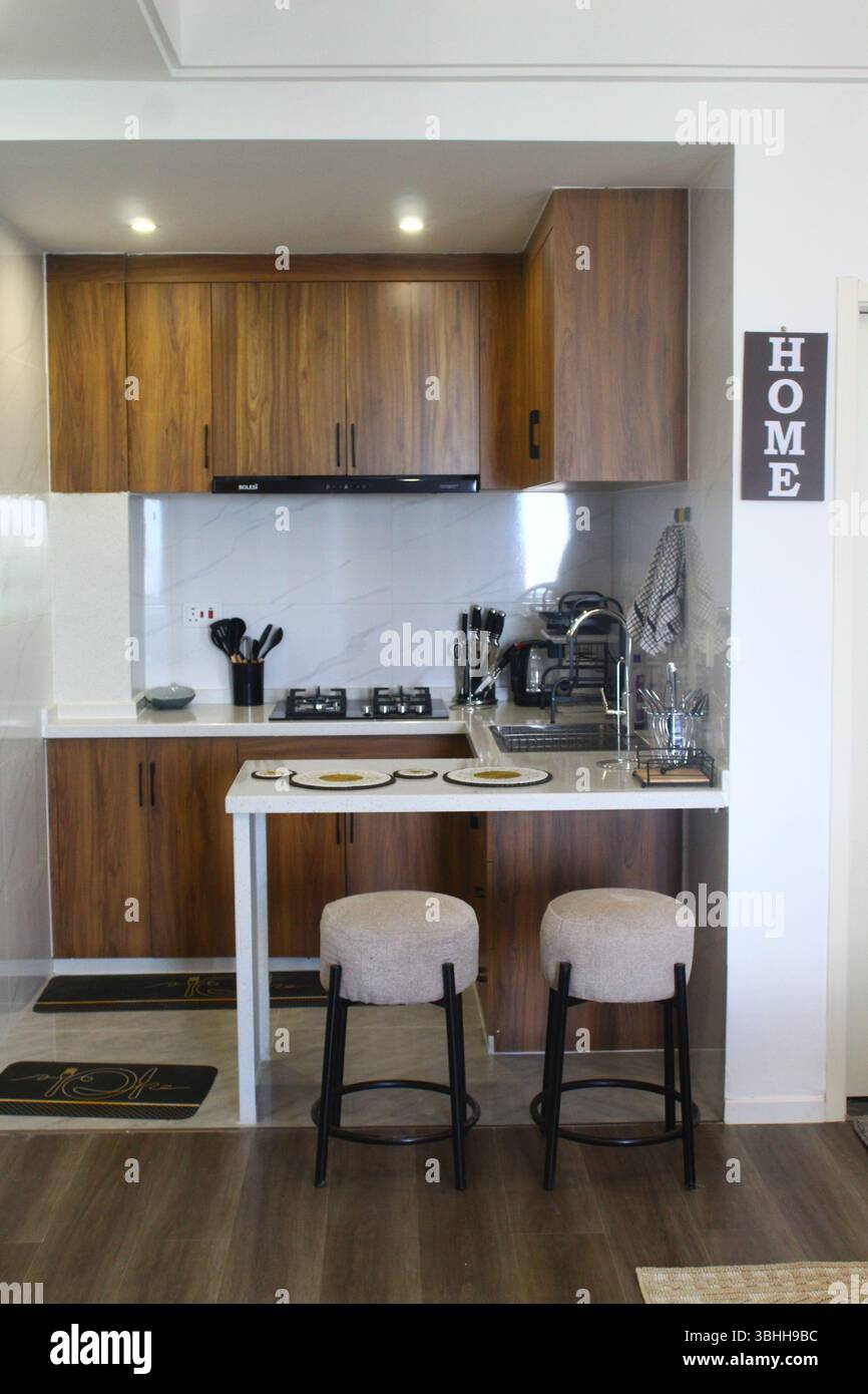 Cucina moderna e compatta con armadi in legno, ripiani bianchi e bar per la colazione Foto Stock