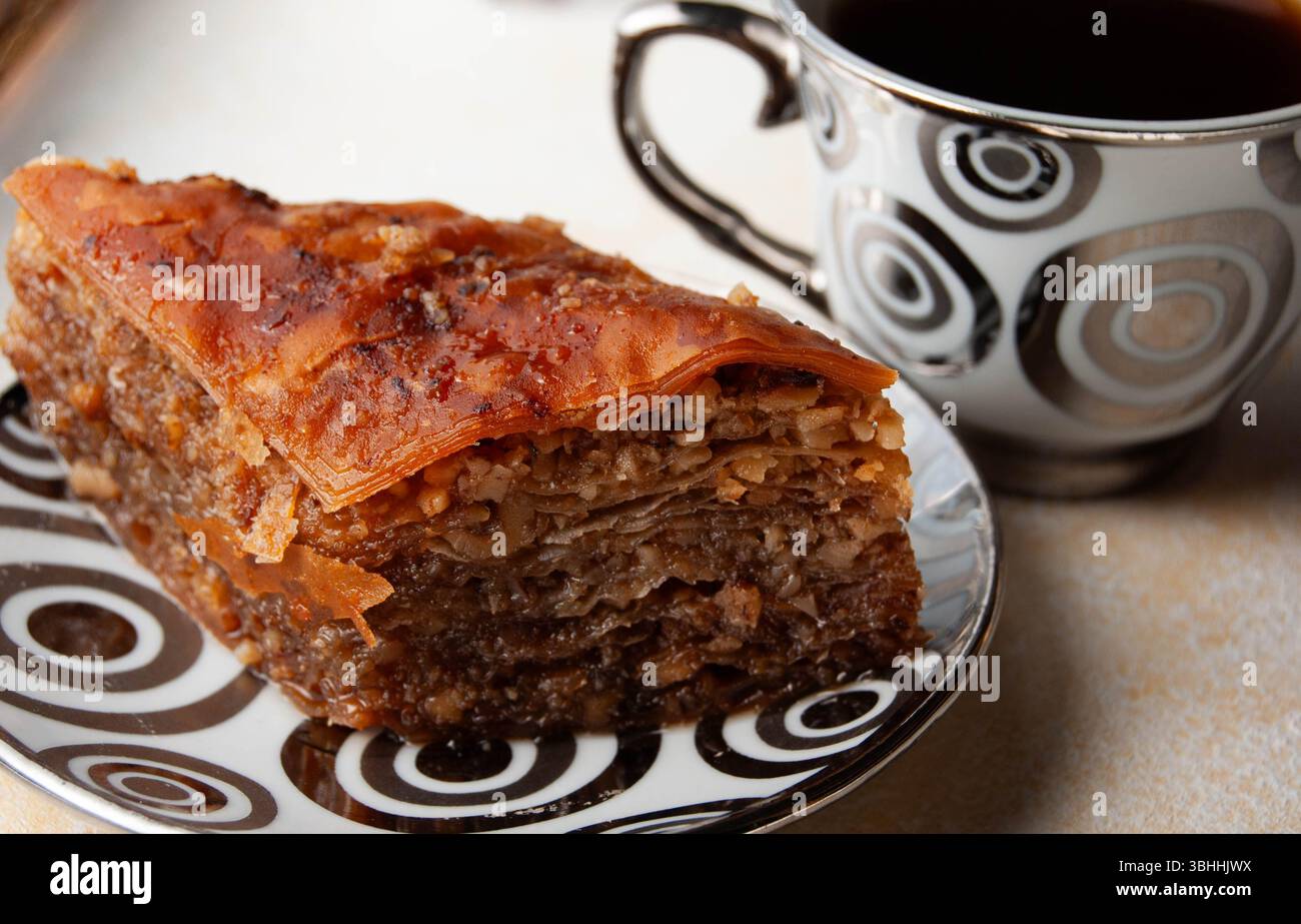 Dolci pezzi di baklava abbinati a una tazza di caffè fumante in un ambiente luminoso. Foto Stock