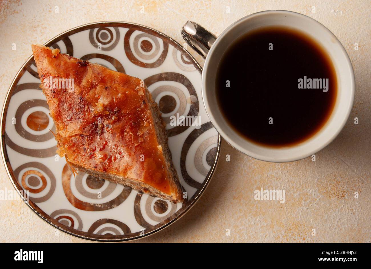 Dolci pezzi di baklava abbinati a una tazza di caffè fumante in un ambiente luminoso. Foto Stock