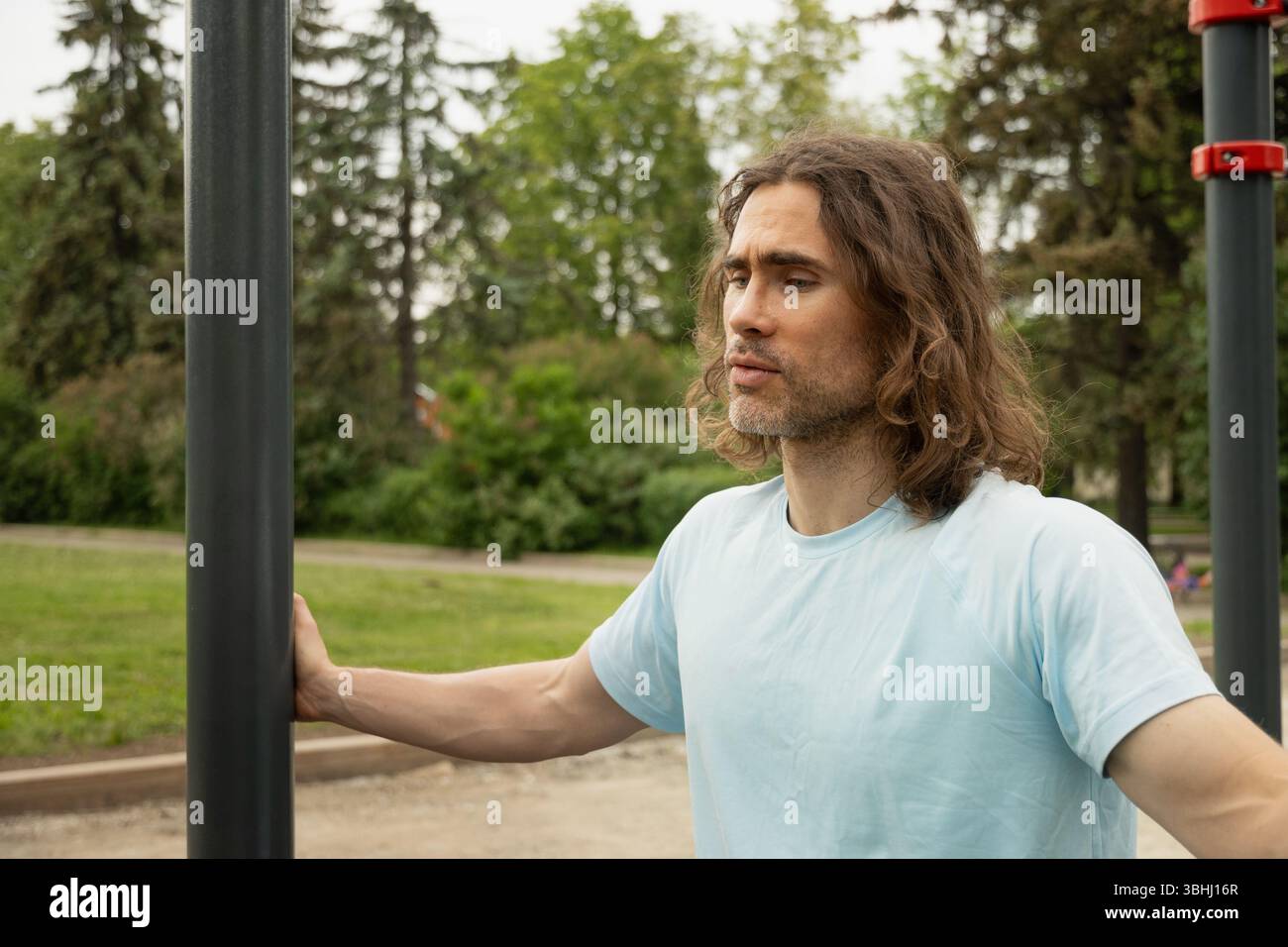 Ritratto di un uomo caucasico stanco e sportivo espressione premurosa, perso nel pensiero nel parco pubblico vicino alle attrezzature sportive. Pigrizia, si obbliga a farlo Foto Stock