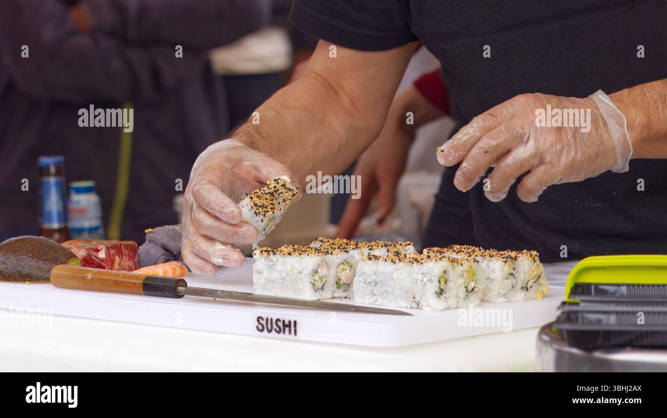 Lo chef che indossa i guanti prepara sushi roll con ingredienti freschi, sottolineando l'igiene e l'abilità degli alimenti. La scena cattura l'arte culinaria, mettendo in mostra Foto Stock