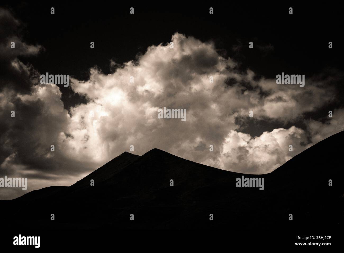 Le maestose montagne formano un contorno scuro sullo sfondo di nuvole vorticose illuminate dal crepuscolo. Sancy Massif in Alvernia . Francia Foto Stock