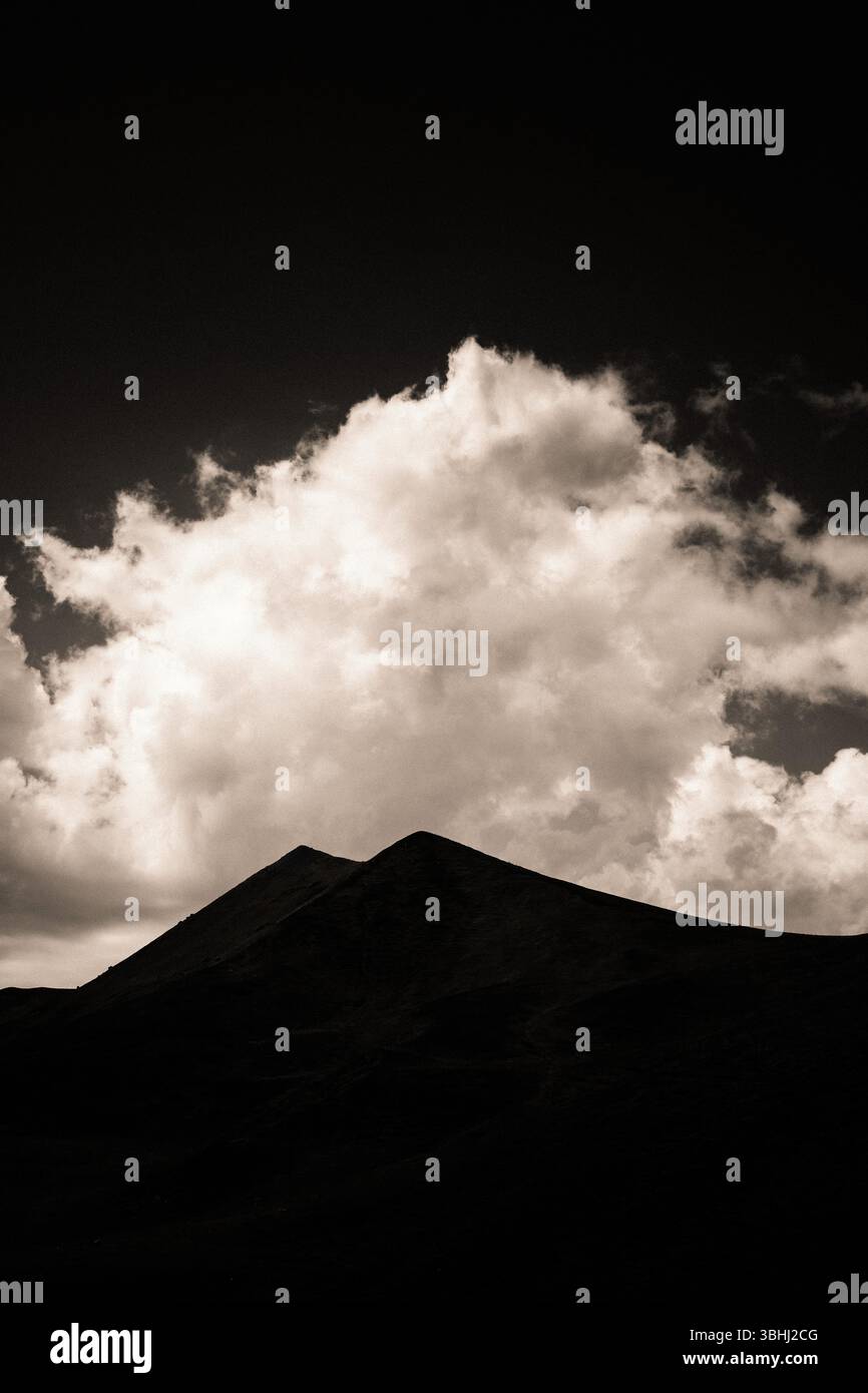 Le maestose montagne formano un contorno scuro sullo sfondo di nuvole vorticose illuminate dal crepuscolo. Sancy Massif in Alvernia . Francia Foto Stock