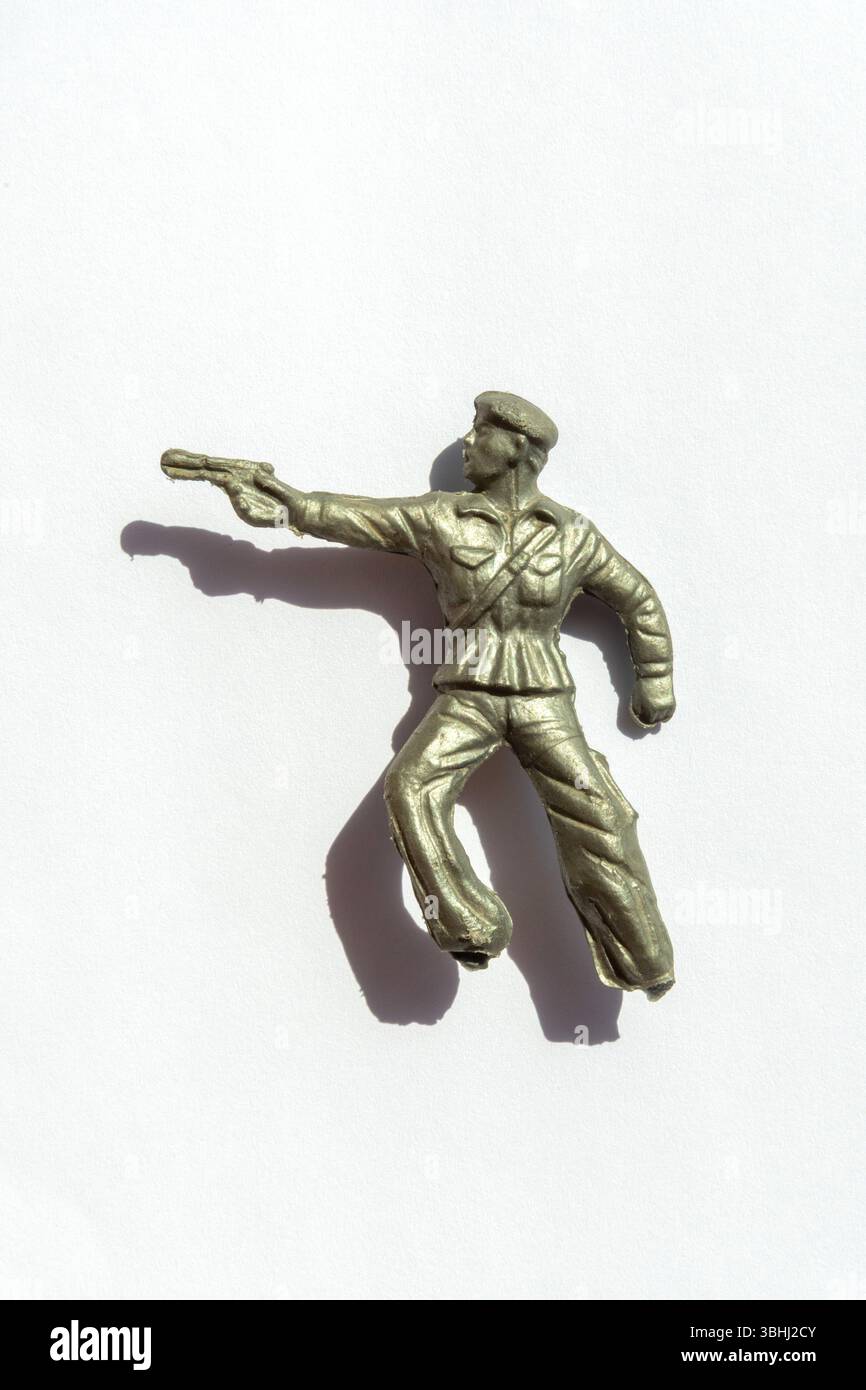 Una piccola figura di plastica verde da soldato è raffigurata puntando una pistola con un'espressione intensa. Foto Stock