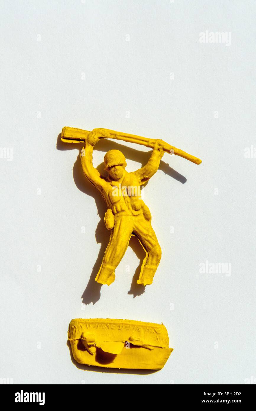 Un soldato giocattolo giallo brillante tiene un fucile sopra la testa, mostrando una posizione imponente. La figura si distingue su un semplice sfondo bianco Foto Stock