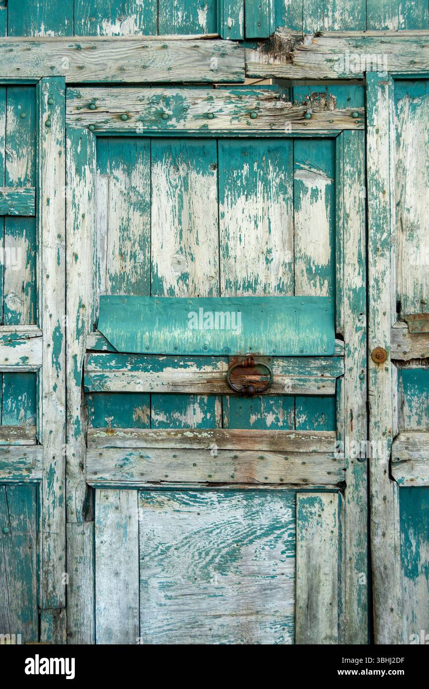 La porta in legno resistente agli agenti atmosferici è caratterizzata da vernice verde acqua e texture ruvide, a testimonianza del suo fascino rustico e dell'età. Foto Stock