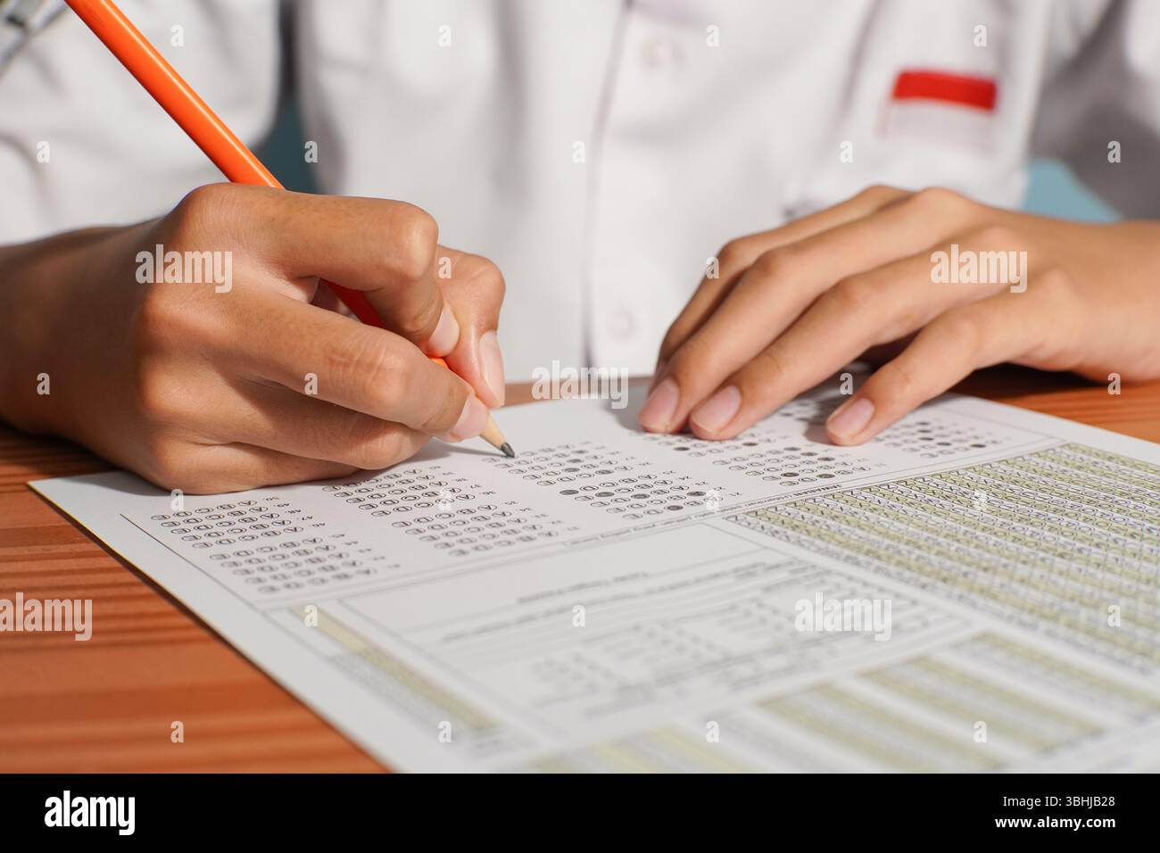 Primo piano di uno studente indonesiano che compila un foglio di risposte a scelta multipla con una matita durante un esame accademico. Nessuna faccia visibile. Foto Stock