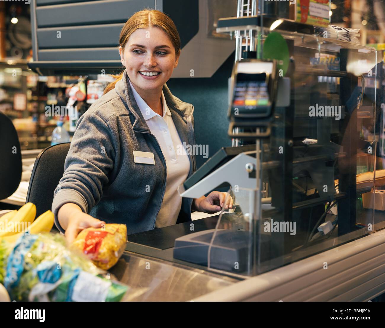 Cassiera sorridente che lavora al registratore di cassa e sposta i prodotti scansionati Foto Stock