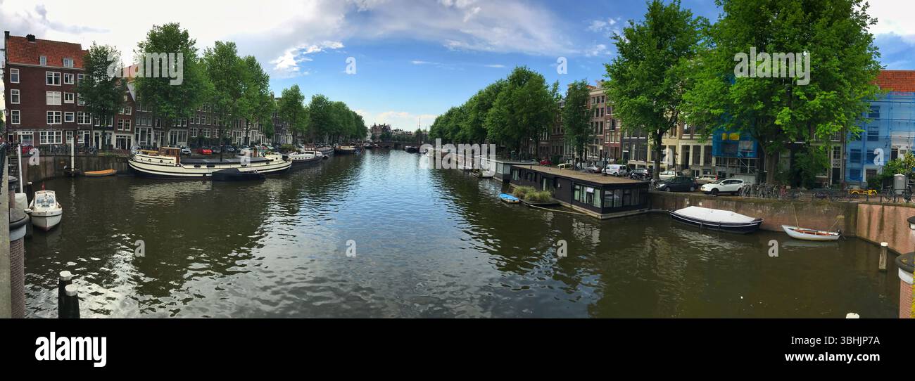 Ampia ripresa di un tranquillo canale fiancheggiato da alberi, barche ancorate e affascinanti case a schiera, creando un tranquillo paesaggio urbano perfetto per la tranquillità e la tranquillità Foto Stock
