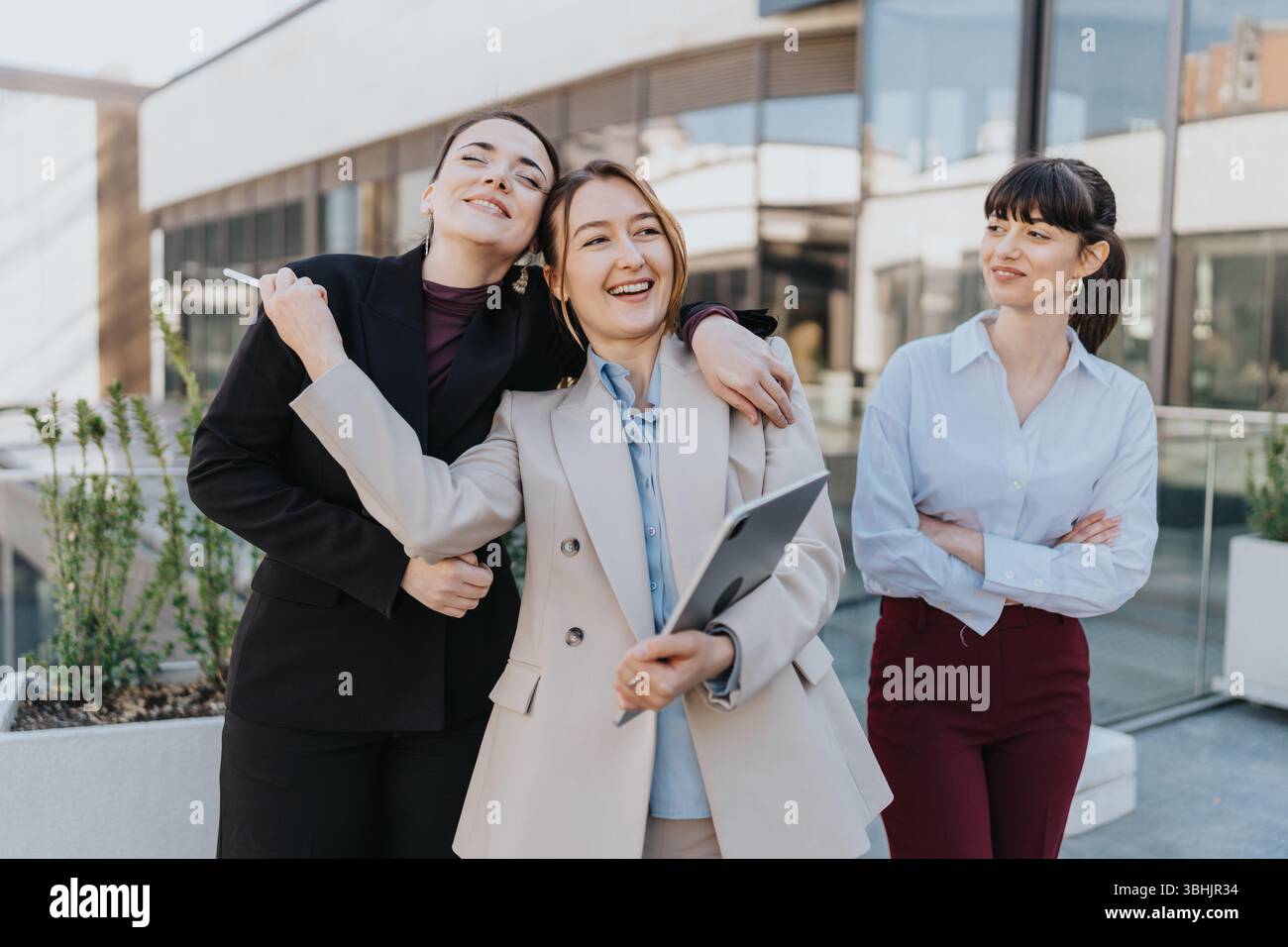 Tre donne professionisti che condividono un momento all'aperto vicino a un moderno edificio per uffici Foto Stock