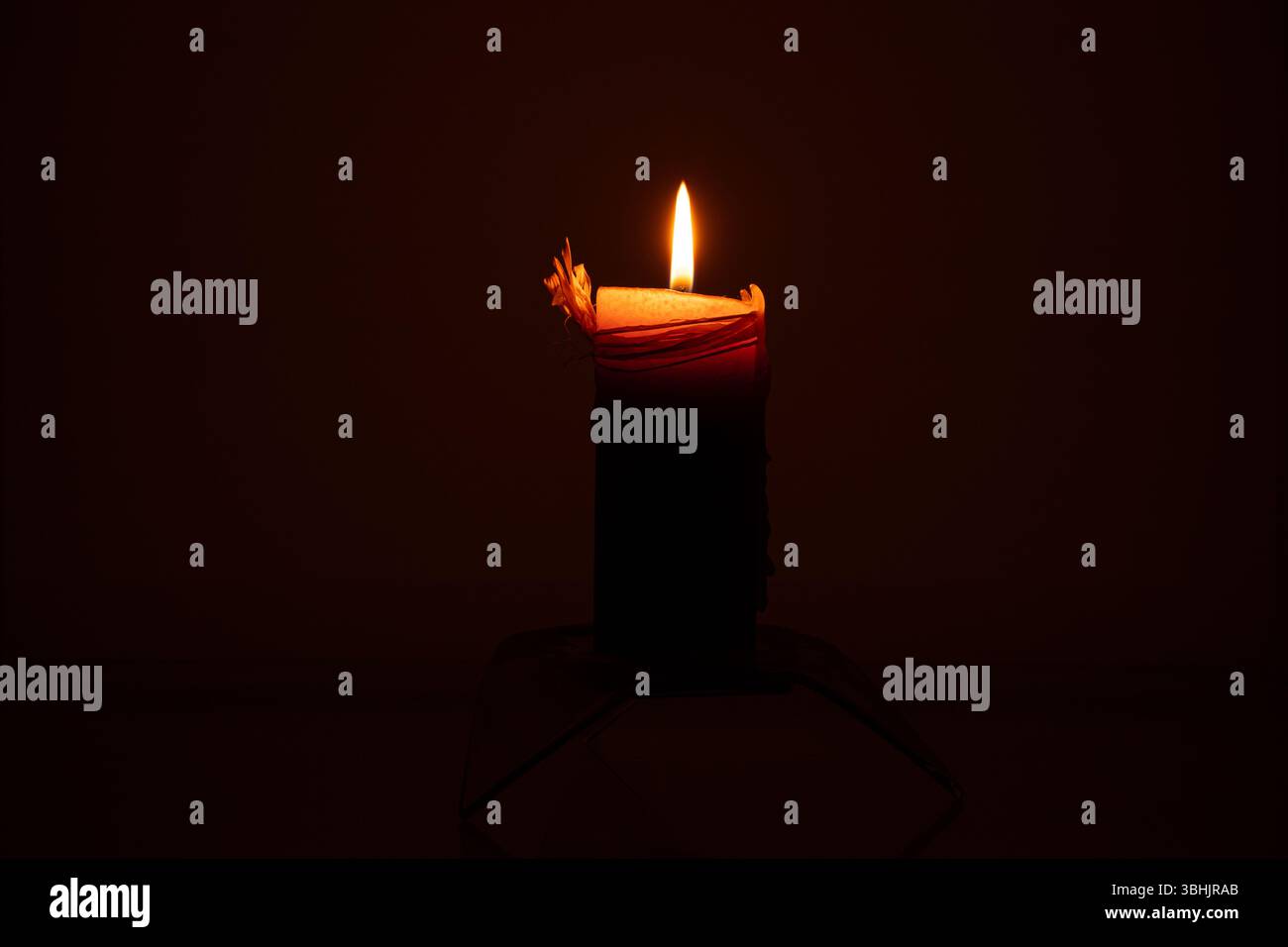 Candela accesa al buio su un piedistallo di vetro, fiamma di candela, primo piano su sfondo scuro, illuminazione serale Foto Stock